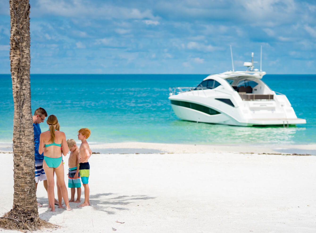 Four kids talking on the beach with a Galeon yacht just off the shoreline