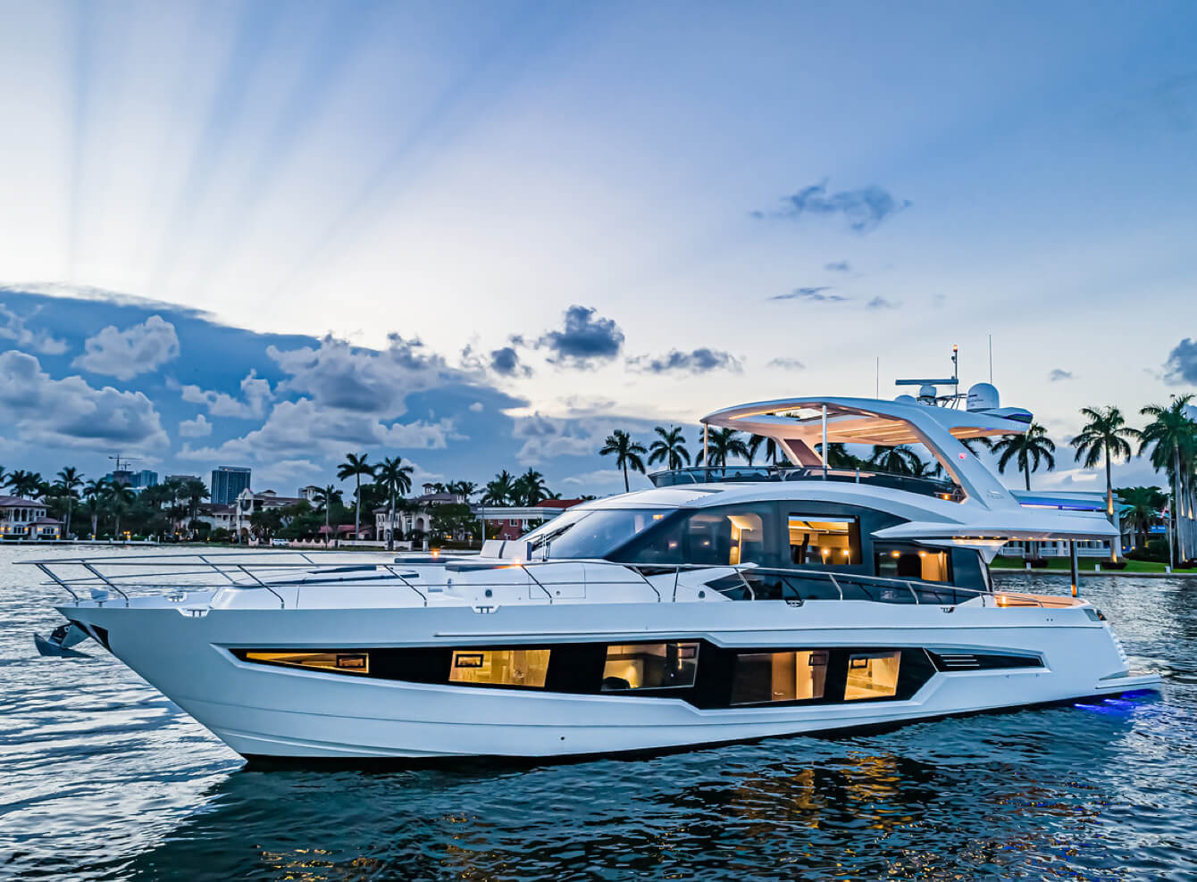 Galeon yacht sitting on the water at sunset with interior lights on and sun rays in the sky