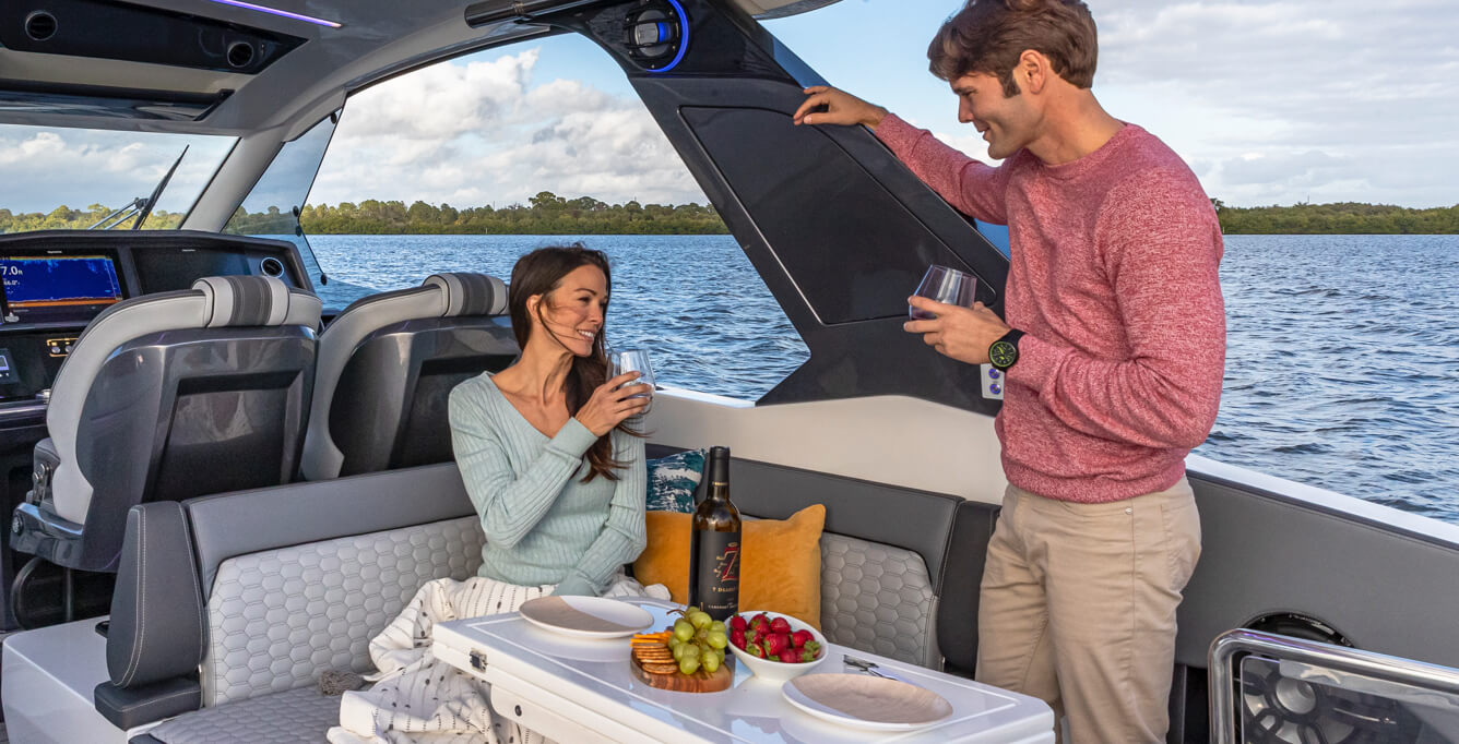 A Galeon yacht cruising on the open water with tall buildings on the shoreline at sunset