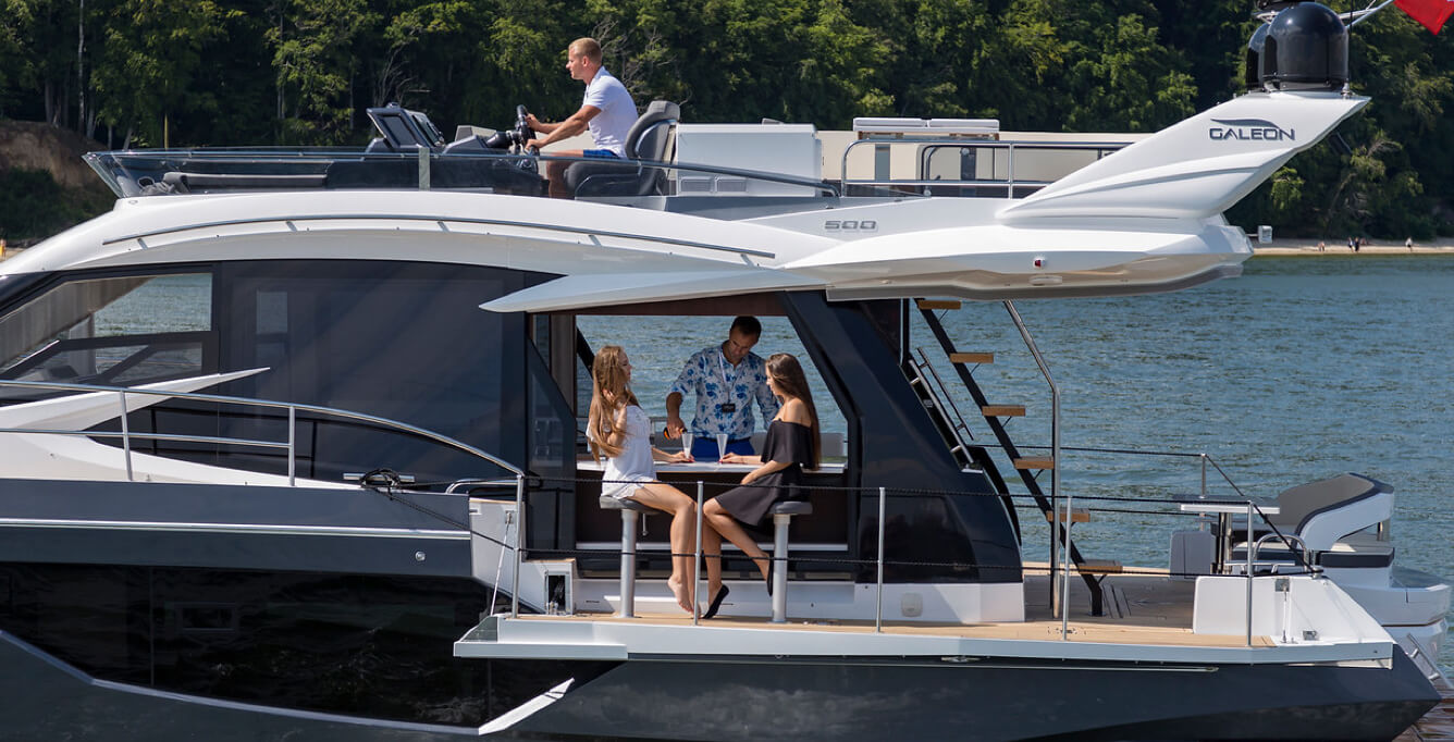 A driver on the top deck of a Galeon yacht and three people at the bar on the deck extension