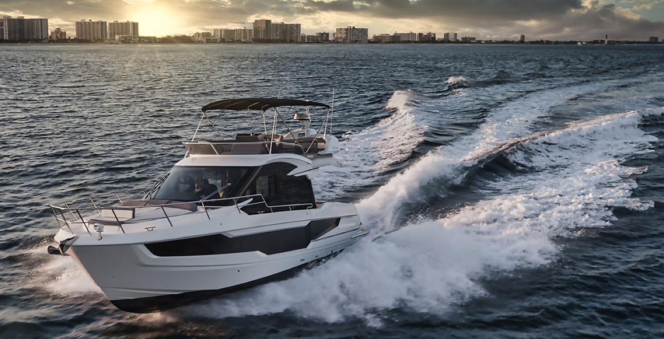 Galeon yacht speeding away from a shoreline of tall buildings at sunset