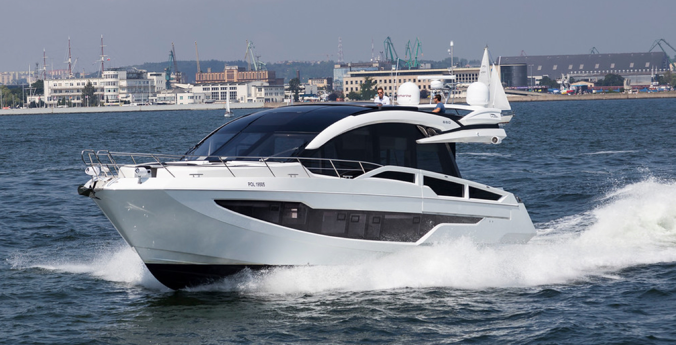 Galeon yacht speeding on the water with buildings all along the shoreline behind it