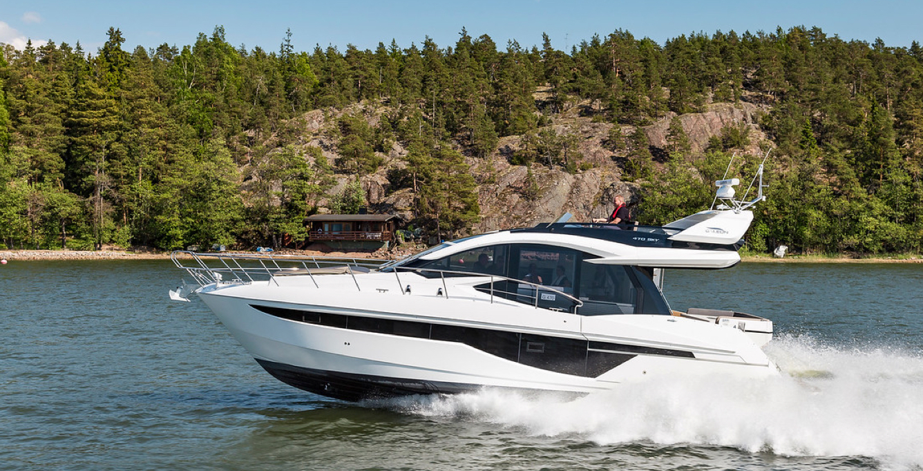 Galeon yacht speeding on open water by a shoreline of rocks and trees