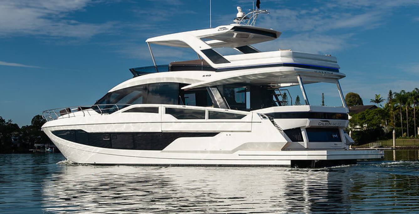 The port side of a Galeon yacht with a white exterior and trees on the shoreline