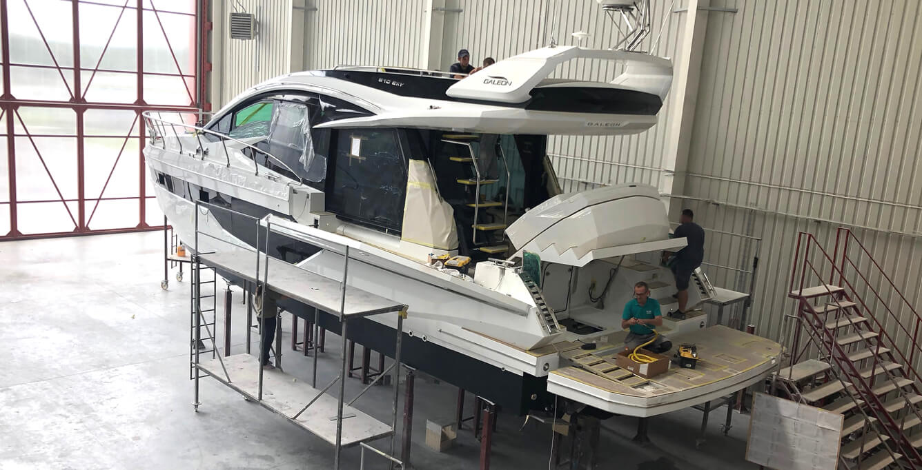 People working to build a Galeon yacht with two people at the stern and two on the starboard side