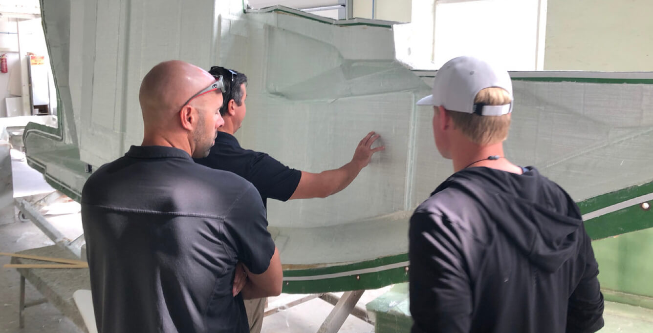 Three people looking at a large piece of a Galeon boat during construction
