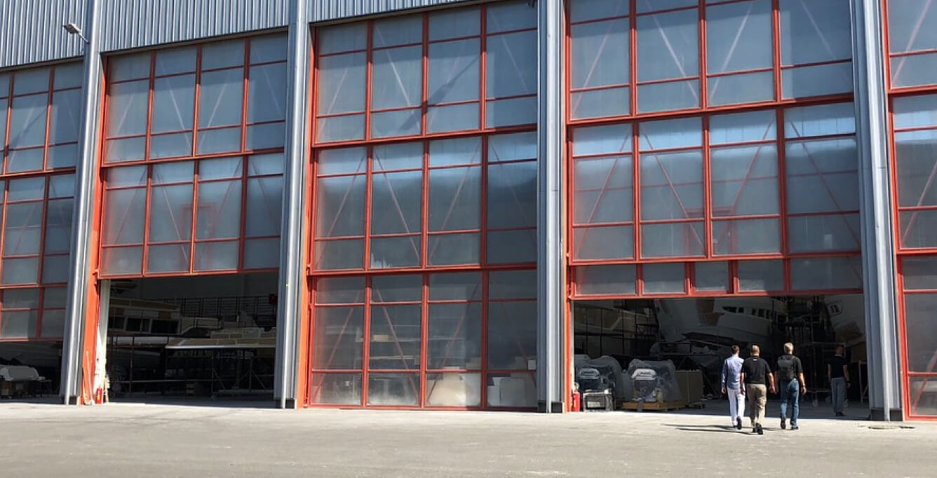 Three people walking toward a warehouse's large, open garage doors with windows