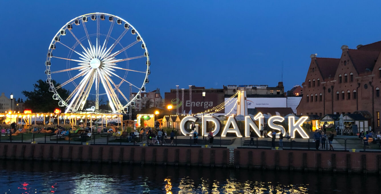 View of the shoreline of Gdansk, Poland at night with lights and a ferris wheel in background