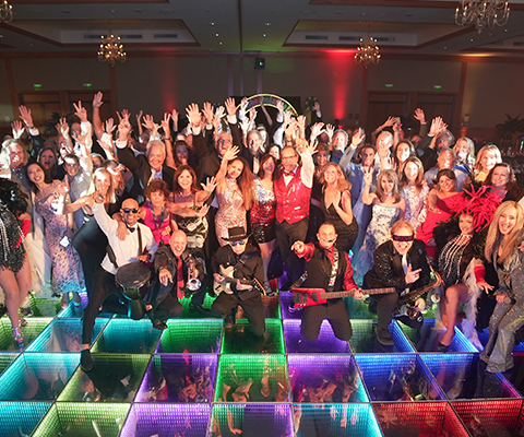 A vibrant group poses energetically on a colorful, illuminated dance floor at the 2025 Galeon Owners Rendezvous.
