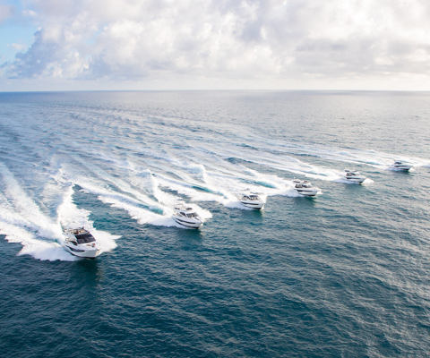 Six Galeon yachts being driven at the same speed on open water on a cloudy day