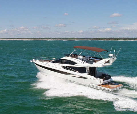 Galeon yacht cruising on open water with a dark shade over the top deck and railings at the bow