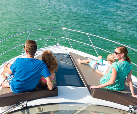 Two adults and two kids sitting on the bow of a Galeon yacht on tan cushions as they look at the water