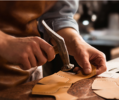 Closeup of a person hammering a piece of tan leather on a table