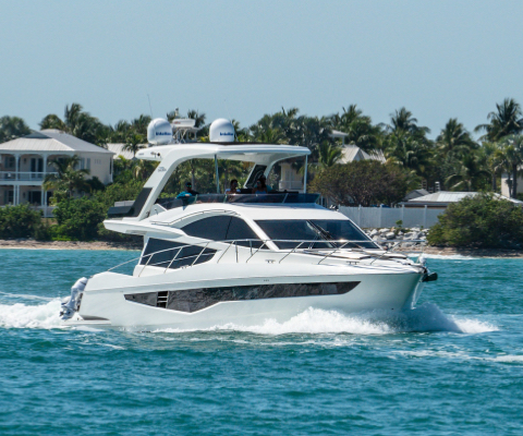 Galeon yacht cruising on light blue water with a house and palm trees on the shoreline