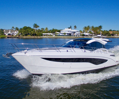 A Galeon hardtop sport yacht moving by houses and palm trees on the shoreline