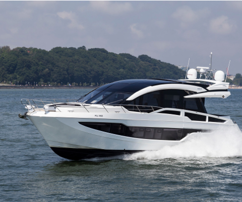 A Galeon sky deck yacht cruising on open water by a shoreline of trees